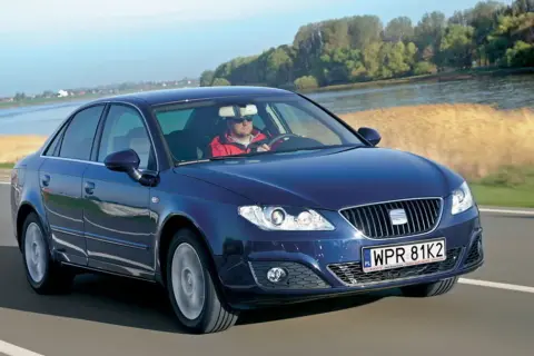 Ciemnoniebieski Seat Exeo 2.0 TDI jedzie drogą nad rzeką, kierowca w czerwonej kurtce.