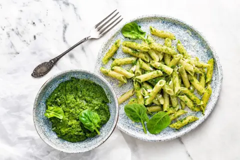 Penne z domowym pesto ze szpinaku, podane w miseczce i na talerzu, z widelcem obok.