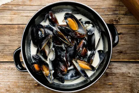 Un plat de moules à la crème, prêtes à être dégustées sur une table en bois rustique.