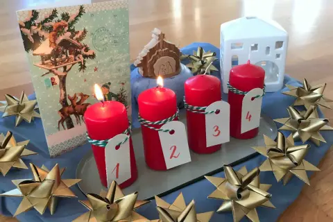 Vier rote Kerzen mit Zahlen 1-4, ein Adventskalender, ein Krippenspiel und goldene Sterne schmücken den Tisch. Perfekt für die Vorfreude auf Weihnachten in der **Advent Grundschule**.