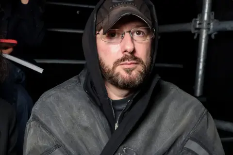 Uomo con cappuccio e cappellino Balenciaga, occhiali e barba, pronto per la sfilata Gucci.