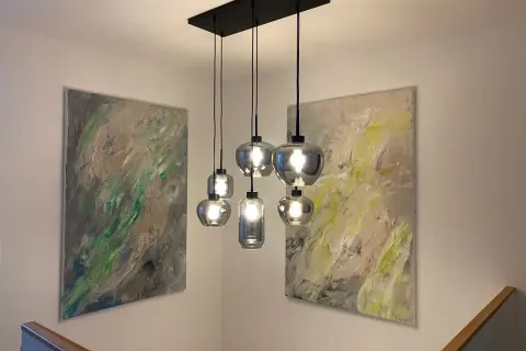 Moderne Hängelampen montieren über einem Treppenaufgang, flankiert von abstrakter Kunst.