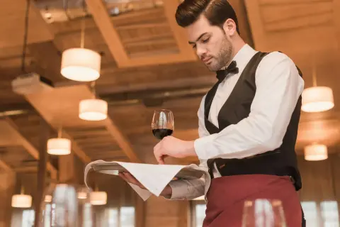 Elegancki kelner, kod zawodu: profesjonalista w białej koszuli i czarnej kamizelce, podaje kieliszek czerwonego wina na tacy.