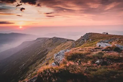 Zachód słońca nad pasmem górskim. Grupa turystów na szczycie, podziwiająca widok. Piękne, jakie góry!