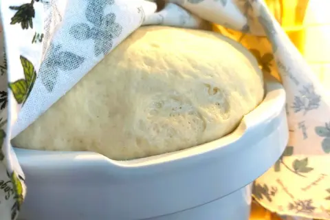 Puszyste ciasto drożdżowe rośnie pod lnianą ściereczką. Idealny czas, ile powinno rosnąć ciasto drożdżowe, to moment, gdy podwoi objętość.