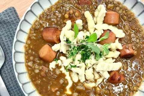 Herzhafte Linsen mit würzigen "Spotzen" (Spätzle) und Fleischwurststücken, garniert mit frischen Kräutern.