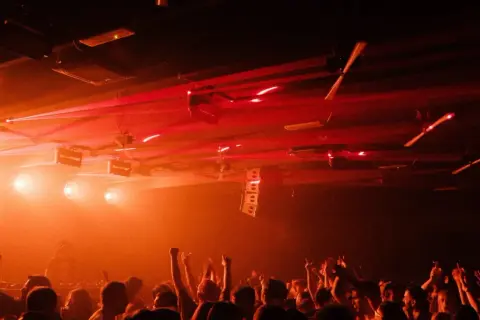 Folla in delirio in una delle tante discoteche techno, con luci laser rosse che illuminano la scena.