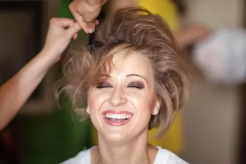 Lachende Frau, der die Haare toupiert werden für einen voluminösen Look.