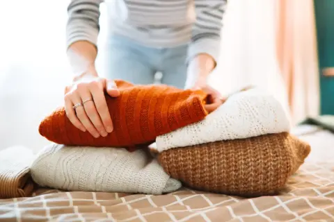 Hände falten warme Pullover. Der Wollprogramm-Waschgang ist abgeschlossen, die Kleidung ist bereit für den Schrank.