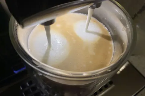 Mleko wylewa się z dyszy ekspresu DeLonghi, tworząc piankę na kawie. Niestety, ekspres DeLonghi nie spienia mleka tak, jak powinien.