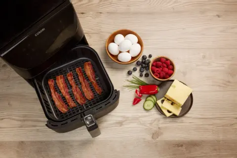 Krispigt bacon i airfryer, redo för en god frukost med ägg, bär och ost.