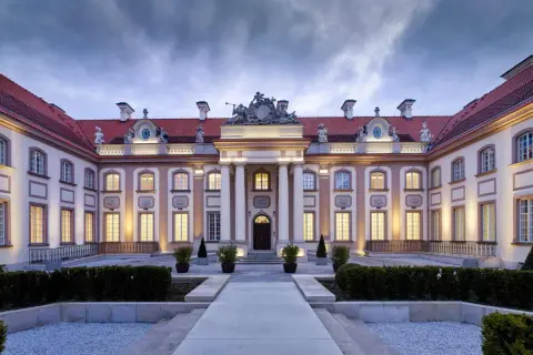 Elegancki pałac z czerwonym dachem i oświetlonymi oknami, wieczorem.