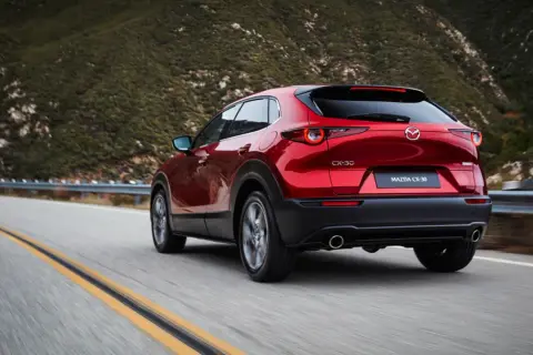 Röd Mazda CX-30 hybrid på en slingrig väg i bergen. Testkörning av den nya modellen.