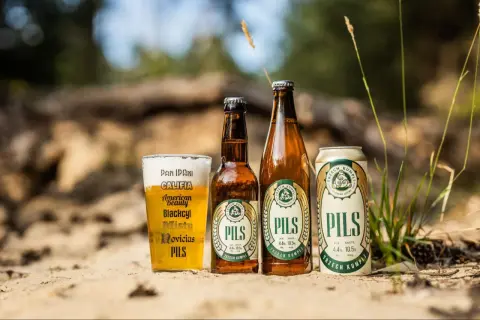 Szklanka i butelki z polskimi piwami typu lager "Pils" od Trzech Kumpli na piasku.