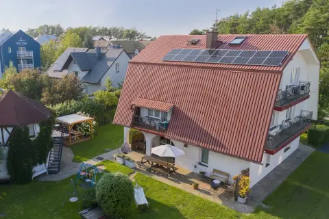 Idealne chłopy noclegi przy plaży: dom z ogrodem, placem zabaw, hamakiem i grillem. W tle widać inne budynki i las.