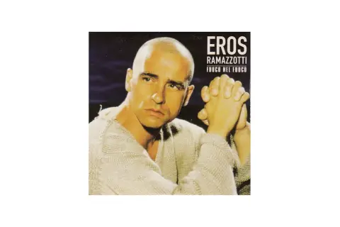 Eros Ramazzotti w swetrze, z dłońmi złożonymi w geście modlitwy. Okładka albumu "Fuoco nel fuoco".