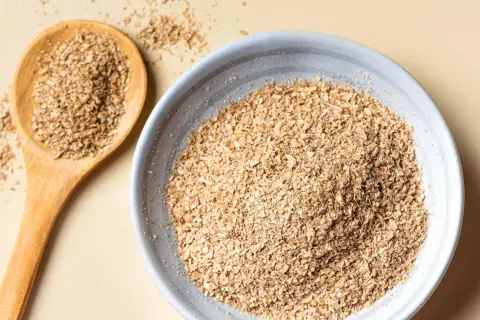 Eine Holzschale und ein Löffel gefüllt mit Haferkleie. Haferkleie ist ein nährstoffreiches Nebenprodukt der Haferverarbeitung.