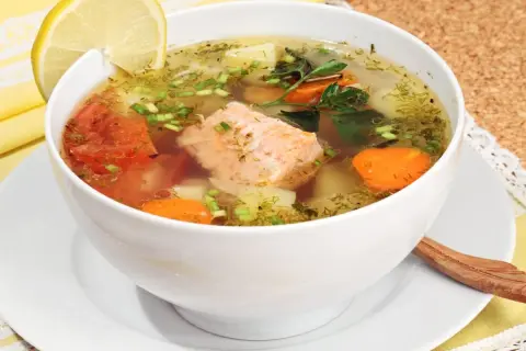 Aromatic rosyjska zupa rybna z łososiem, ziemniakami, marchewką i pomidorami, ozdobiona cytryną i koperkiem.