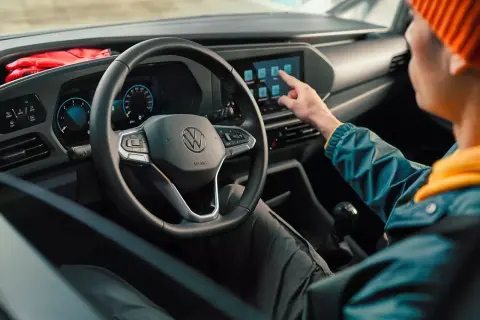 Interni moderni del Volkswagen Caddy: un utente interagisce con il touchscreen centrale, mentre il volante e il cruscotto digitale sono ben visibili.