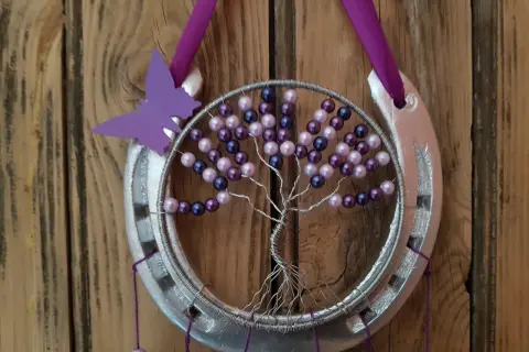 Tuto attrape rêve arbre de vie : un fer à cheval argenté orné d'un arbre de vie en fil de fer et perles violettes et roses, avec un papillon violet.