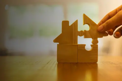 Mano aggiunge un pezzo a un puzzle a forma di casa, simboleggiando una casa in comproprietà tra fratelli e madre.