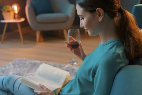 Kobieta z kieliszkiem wina czyta książki. Może to być jedna z fascynujących powieści Joanny Jax, która wciąga w swój świat.