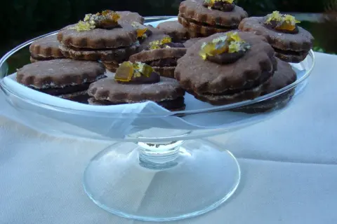 Gourmandes bouchées de biscuits fourrés chocolat, ornées de zestes d'agrumes confits, présentées dans une coupe en verre.