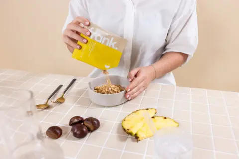 Frau gibt Müsli in eine Schüssel. Das ist Teil der Intervallfasten Regeln für ein gesundes Frühstück.