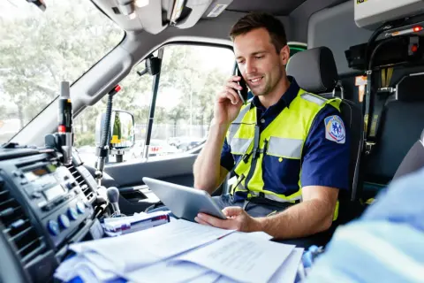 Paramédic en uniforme, parlant au téléphone et consultant une tablette dans un véhicule prioritaire, respectant le code de la route.