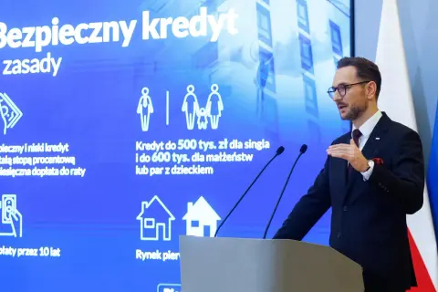 Mężczyzna w garniturze prezentuje zasady "Bezpiecznego kredytu" z dopłatą do rat. Program oferuje kredyt 2 procent dla singli i małżeństw.