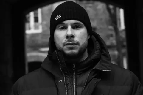 Portret młodego mężczyzny w czapce z logo Lacoste, jednego z wielu polskich raperów, który tworzy muzykę uliczną.