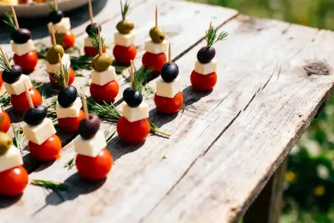Des mini brochettes apéritives sans cuisson : tomates cerises, dés de fromage, olives noires et vertes, garnies de romarin frais sur une table en bois.