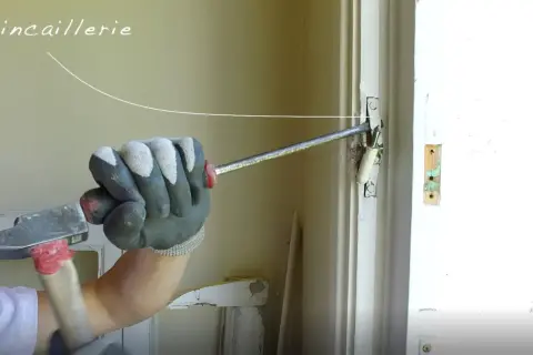 Main tenant utilise un marteau pour ajuster la quincaillerie d'une porte, travaillant sur une pose en feuillure.