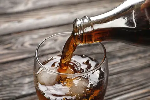Nalewanie ciemnego napoju z butelki do szklanki z lodem. Zastanawiasz się, ile kalorii ma whisky z colą zero?