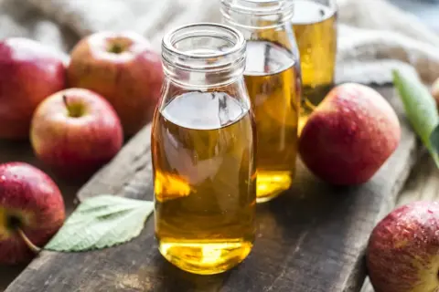 Frische Äpfel umgeben zwei Flaschen mit goldenem Apfelessig. Ein gesundes Elixier, das aus Früchten gewonnen wird.