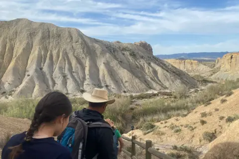 Senderos del desierto de Almería, con formaciones rocosas erosionadas y vegetación escasa. Un grupo de excursionistas se adentra en el paisaje.