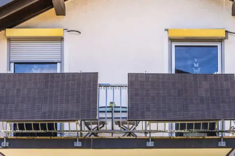 Dwa panele fotowoltaiczne na balkonie, symbolizujące odnawialne źródła energii w domu. Obok kwitnące kwiaty.