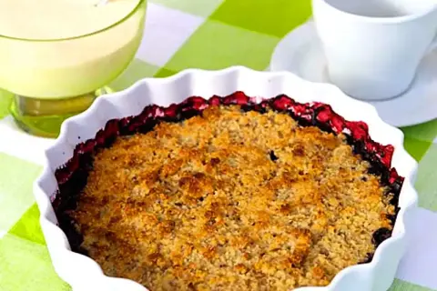 En gyllene glutenfri smulpaj med bär, serverad med vaniljsås.