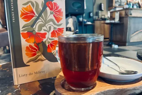 Kawa i książka "Listy do Mileny" Franza Kafki na stoliku w kawiarni.