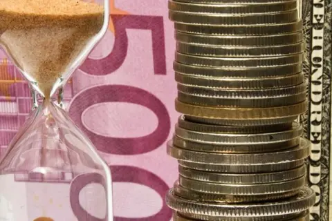 Klepsydra i stos monet na tle banknotu 500 euro. Czy numizmaty co to, to tylko monety?