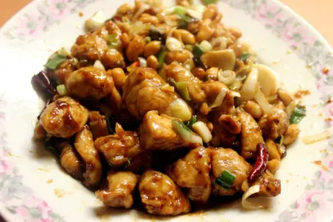 Kurczak Gong Bao z orzeszkami ziemnymi, cebulą i papryczkami chili na talerzu.
