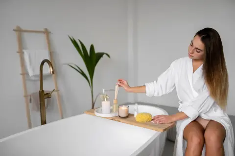 Mujer en bata blanca prepara su **zona de relax** en el baño, con velas, difusor y esponja.