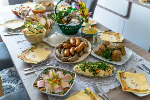 Obficie zastawiony stół z wieloma potrawami, w tym kiełbasami, galaretą i sałatkami. To idealne przystawki na Wielkanoc.