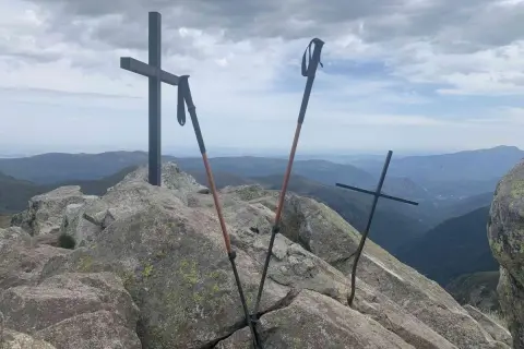 Sommet du pic des 3 Seigneurs. Deux croix et des bâtons de randonnée sur un rocher, avec une vue panoramique sur les montagnes.
