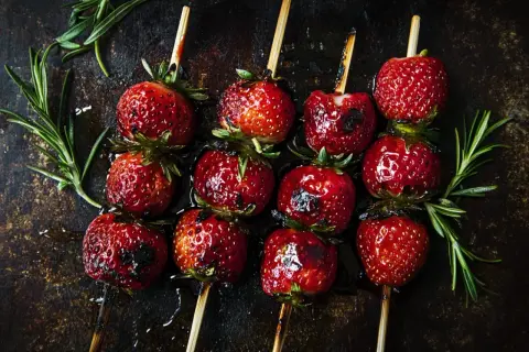 Zuckersüße Erdbeeren auf Spießen, leicht gegrillt und glänzend, mit Rosmarin garniert. Ein Genuss für alle Sinne!