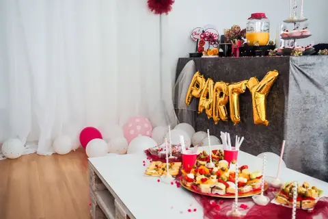 Złote balony z napisem "PARTY" i przekąski na stole tworzą atmosferę wieczoru panieńskiego w domu.