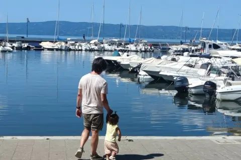 Padre e figlia passeggiano sul lungolago di Bolsena, con barche ormeggiate sullo sfondo.