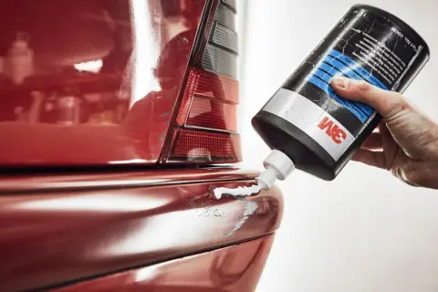 Hand drückt 3M-Paste auf zerkratzten roten Autolack. So lassen sich auto kratzer entfernen und der Glanz wiederherstellen.