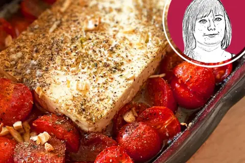 Ein Block Feta mit Kräutern und Gewürzen, umgeben von gebackenen Kirschtomaten. Perfekt für ein schnelles Gericht mit Nudeln mit Feta.