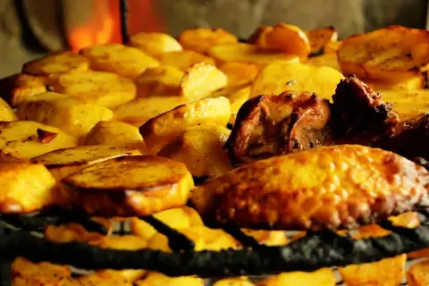 Patatas asadas y carne sobre una parrilla, un delicioso plato de comida típica de Armenia, con fuego al fondo.